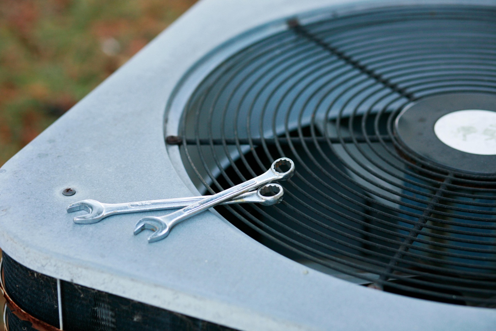Three wrenches are placed on top of an outdoor air conditioning unit near the fan grille, perfect for a landing page header showcasing HVAC repair tools.
