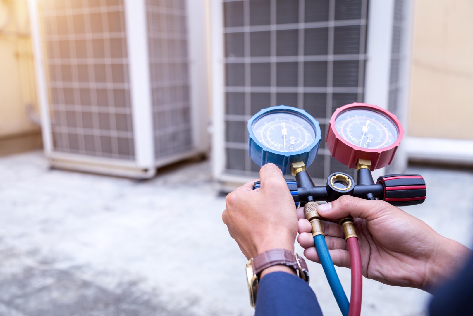A technician holds a set of HVAC manifold gauges, checking air conditioning units outdoors—an ideal image for your landing page header.