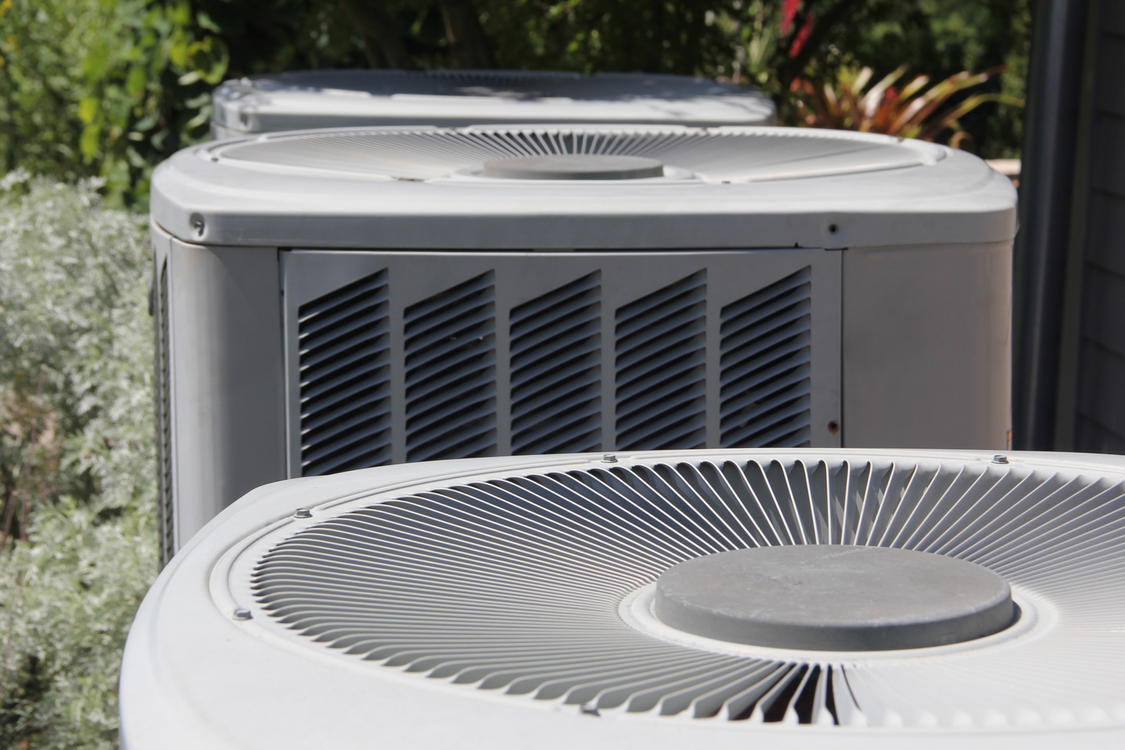 Close-up view of multiple outdoor air conditioning units lined up, perfect for a landing page header, showcasing their top fan covers and metal vent panels.